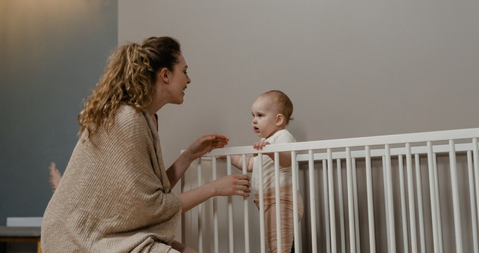 Baby standing in a crib and talking with mom