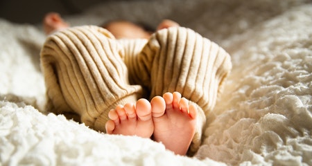 Barefooted baby sleeping on soft bed in sunlight