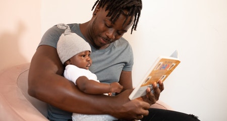 Man is gray shirt holding a baby in white onesie