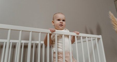 Toddler standing on the write crib