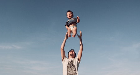 Photo of man in raising a baby under blue sky