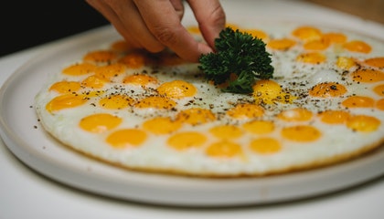 Crop unrecognizable chef garnishing fried eggs with herbs