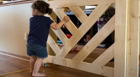 A little girl is standing next to the A DIY wooden baby gate
