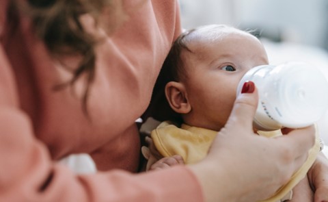 A newborn is drinking milk from the milk feeder