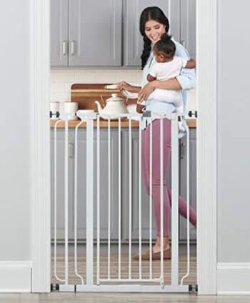 A mom is standing with her daughter next to the Regalo Extra Tall Metal Pet and Baby Gate