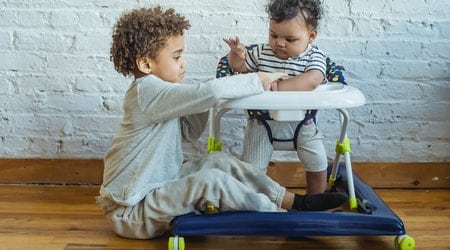 An infant is on the walker and a toddler playing with him