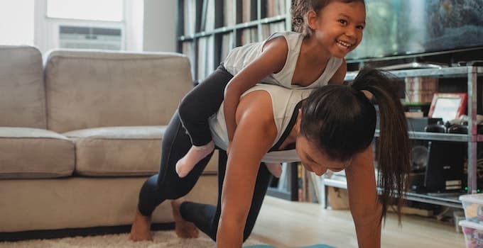 Young Asian woman piggybacking smiling daughter while exercising at home