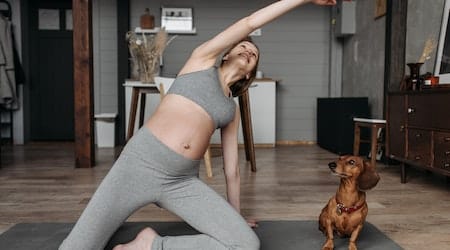 A woman is practicing yoga next to her dog
