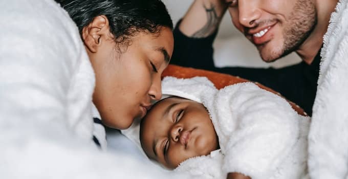Cheerful young multiethnic parents admiring sleeping baby on bed